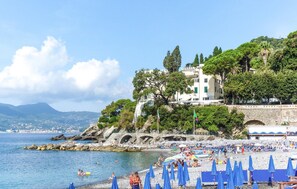 A coastal beach with a stone bridge, beach umbrellas, and a building with a balcony overlooking the sea. - 1 bedroom lovely apartment in Mezzanego (Mezzanego)