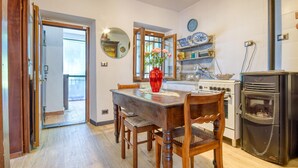 A kitchen with a dining table, chairs, a red vase with flowers, a stove, a microwave, and a clock on the wall. - 1 bedroom lovely apartment in Mezzanego (Mezzanego)