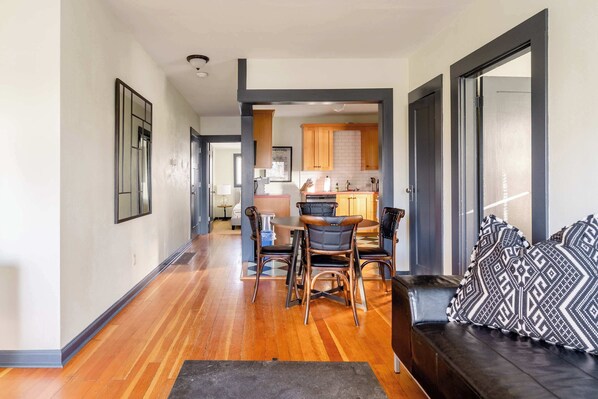 A modern living room with a wooden floor, a black leather sofa, and patterned cushions.