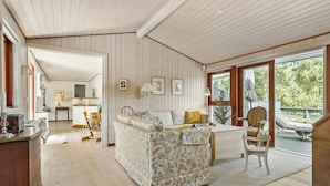 A spacious living room with a floral sofa, wooden flooring, and a large window offering a view of the outdoors.