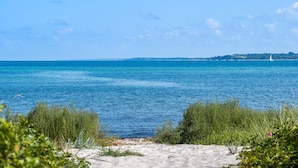 A beach with clear blue water, sandy shore, and distant shoreline with buildings.