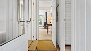 A hallway with white doors, a wooden bench, and a rug leading to a room with a fireplace.