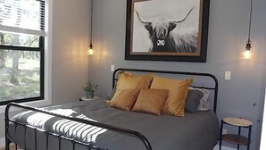 Ein Schlafzimmer mit einem Bett, einem Nachttisch, einem gerahmten Bild an der Wand und einem Fenster mit Jalousien.