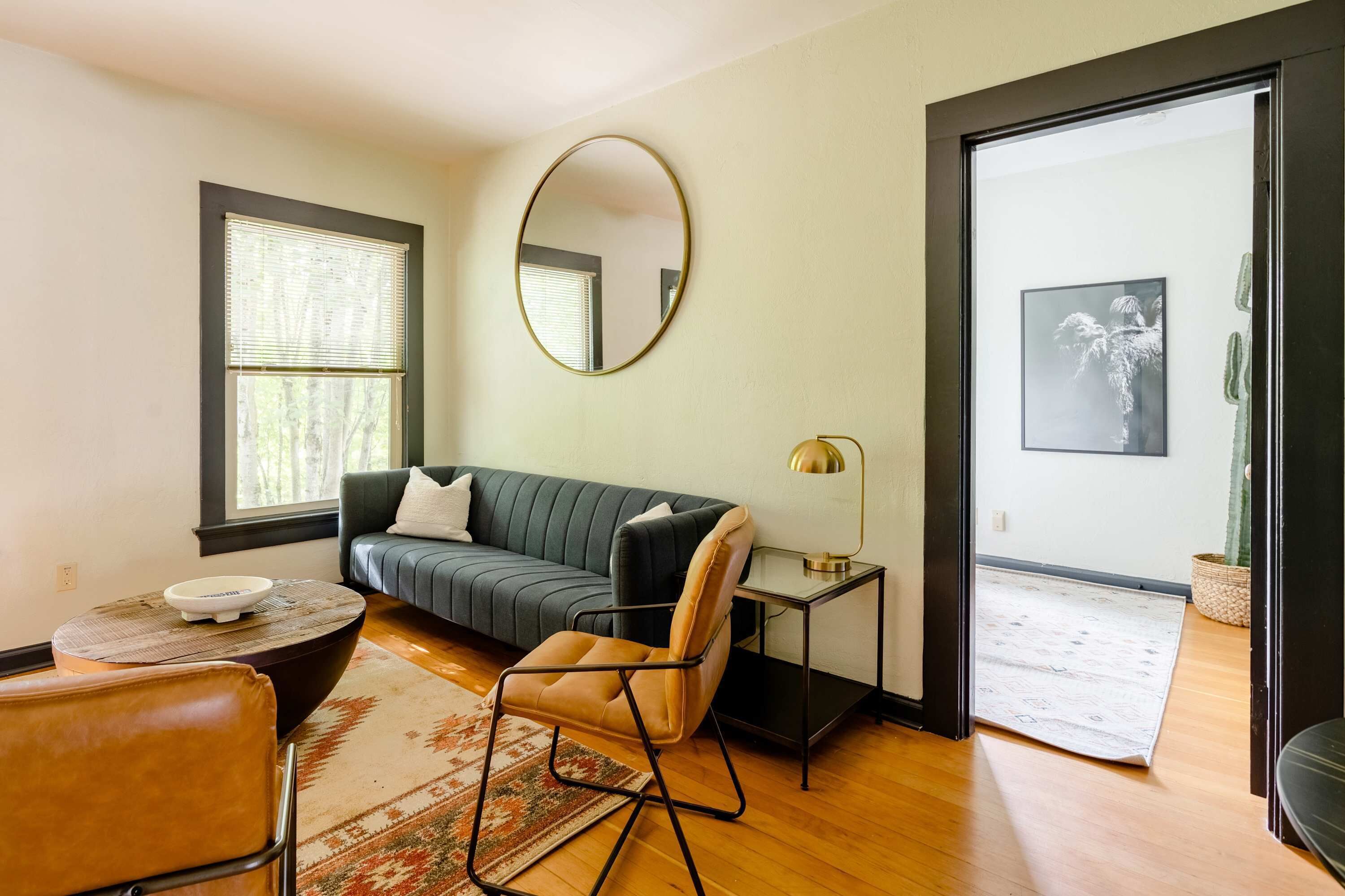 Een woonkamer met een bank, een fauteuil, een salontafel, een lamp en een grote spiegel aan de muur.
