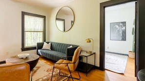 A living room with a sofa, a chair, a coffee table, a lamp, and a large mirror on the wall. - Moab Vibes in PDX - Walk to Local Coffee & Food (Portland)