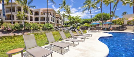 A resort pool area with lounge chairs and a building in the background.