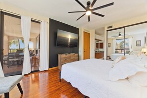 A bedroom with a large bed, a ceiling fan, a TV on the wall, and a sliding glass door leading to a balcony. - Hilton Pool Pass Incl. Serene Resort Gem (Waikoloa)