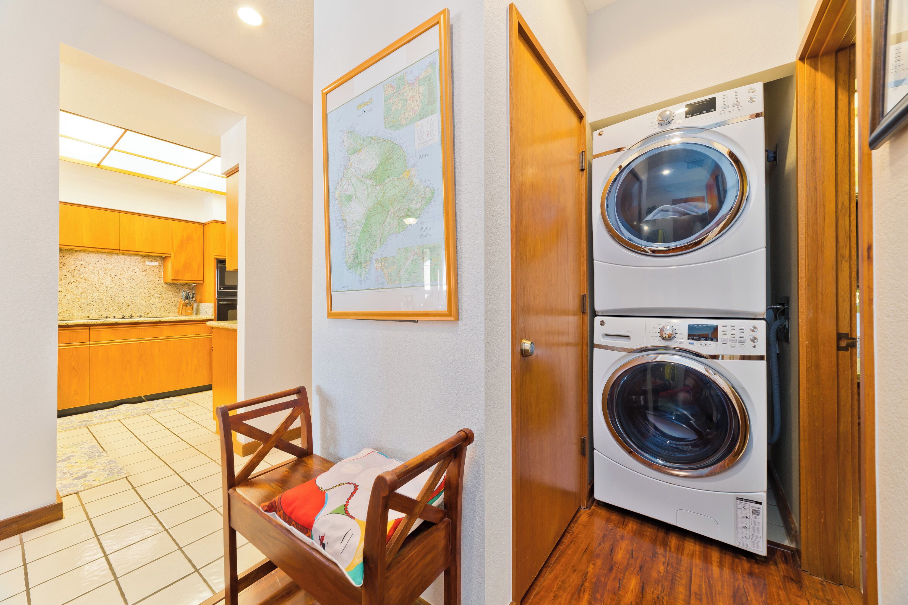 A laundry room with two stacked washing machines, a wooden chair, and a map on the wall.