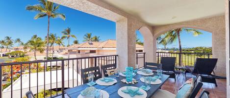 A dining area with a table set for four, outdoor chairs, and a view of palm trees and buildings.