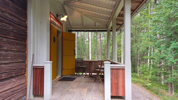 Een houten chalet met een veranda, een gele deur en een tafel met stoelen.