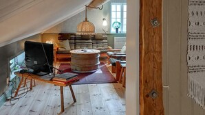 Een gezellige zolderkamer met een houten tafel, boeken, een computer en een hanglamp.