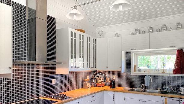A modern kitchen with white cabinets, a wooden countertop, and a black and red tiled backsplash.