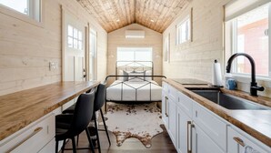 A compact, modern kitchen with a wooden ceiling, a central island, and a large window providing natural light. - The Tiny Farmhouse on Alberta (Portland)