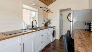 A kitchen with wooden cabinets, a sink, a washing machine, and a dining area with a table and chairs. - The Tiny Farmhouse on Alberta (Portland)