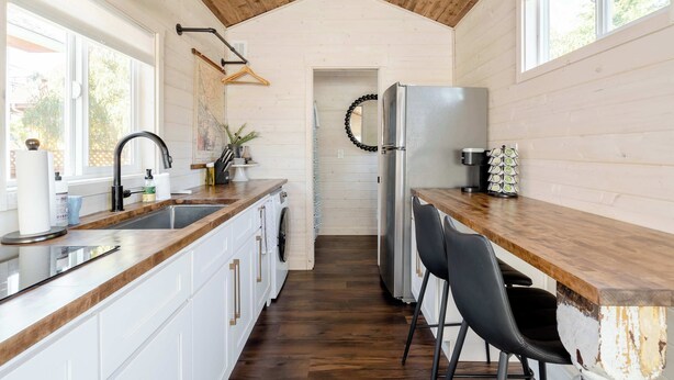 A kitchen with wooden cabinets, a sink, a refrigerator, and a bar counter with chairs. - The Tiny Farmhouse on Alberta (Portland)