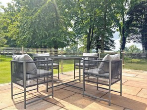 Un patio al aire libre con una mesa redonda y cuatro sillas, rodeado por una barandilla de vidrio.