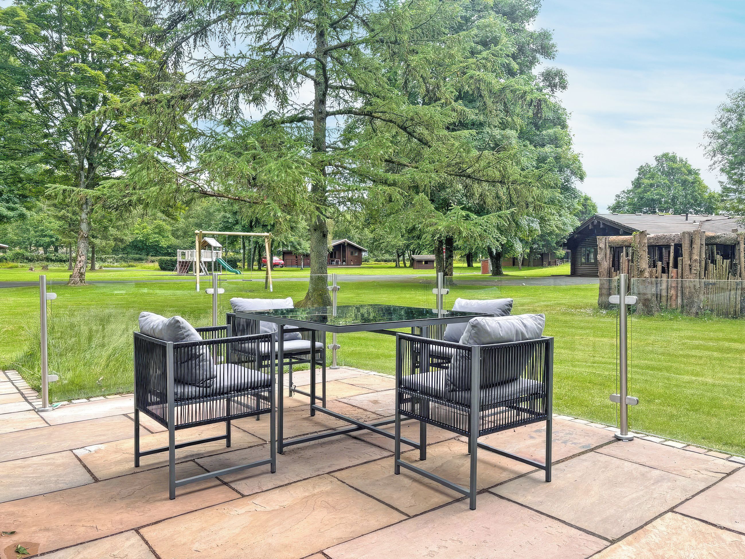 An outdoor patio with a glass-top table and four chairs, surrounded by a stone patio.