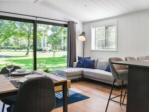 A modern living room with a dining area, large windows, and a view of a park. - 2 bedroom accommodation in Ingleton (Ingleton)