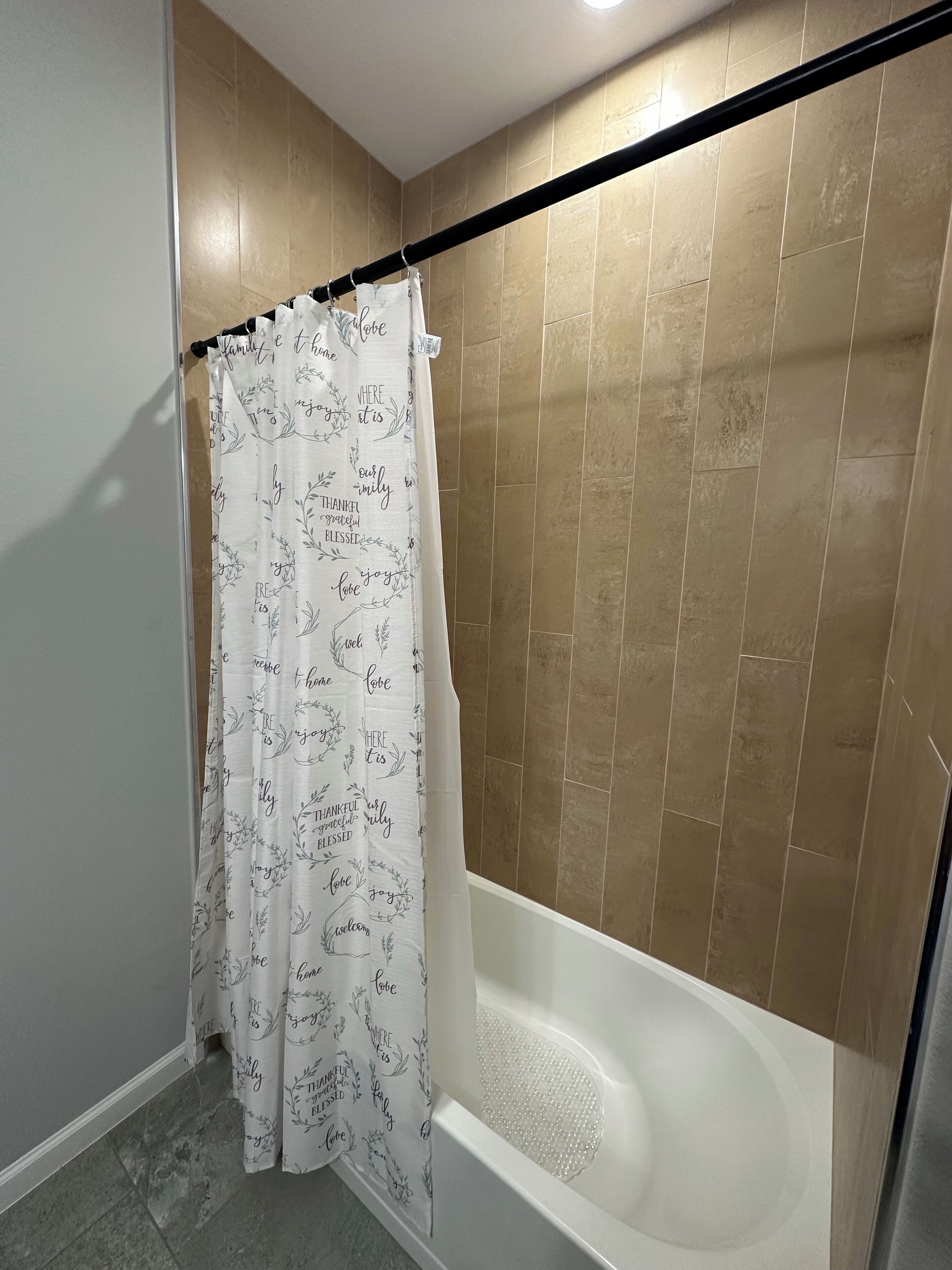 A bathroom with a bathtub, beige tiled walls, and a shower curtain with motivational phrases.