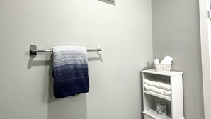 A bathroom with a towel rack, a shelf with towels, and two wall-mounted signs.