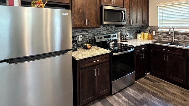 A modern kitchen with dark wood cabinets, stainless steel appliances, and a granite countertop.