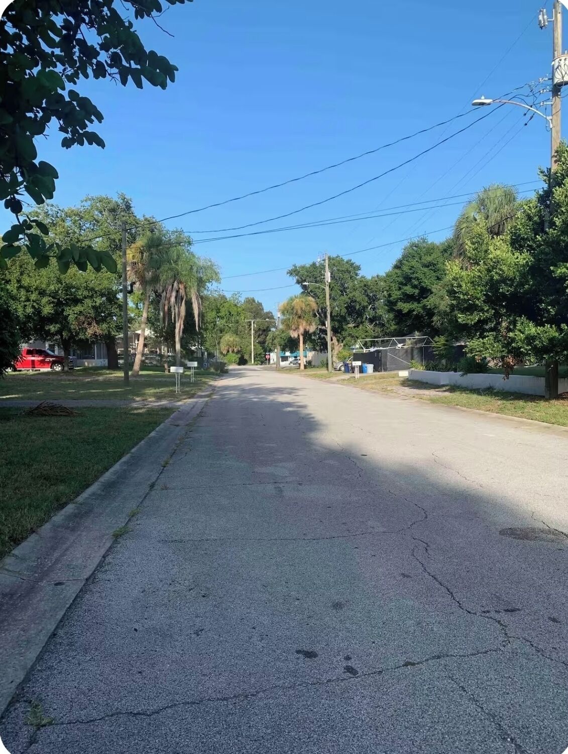 A quiet residential street with houses on both sides, a clear sky, and power lines overhead.