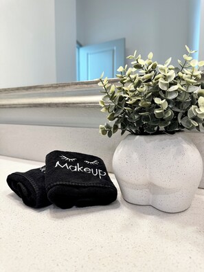 A white vase with a speckled pattern containing green foliage, placed on a countertop next to a black towel with the word "makeup" embroidered on it. - Luxury 2-bedroom Apt minutes from Love Field Airport, Deep Ellum, AT&T District  (Dallas)