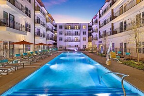 A modern hotel with a central swimming pool, lounge chairs, and a well-lit outdoor area. - Luxury 2-bedroom Apt minutes from Love Field Airport, Deep Ellum, AT&T District  (Dallas)