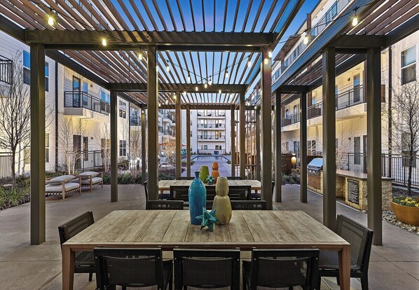 An outdoor patio with a wooden table and chairs, surrounded by a pergola with string lights. - Luxury 2-bedroom Apt minutes from Love Field Airport, Deep Ellum, AT&T District  (Dallas)