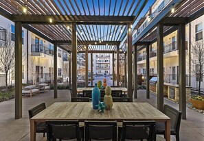 Ulkoterassi, jossa on puinen pöytä ja tuolit, ja jonka ympärillä on pergola, johon on ripustettu valonauhoja.