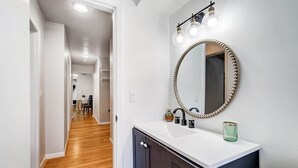 Une salle de bain moderne avec un grand miroir, un lavabo blanc et un revêtement de sol en bois.