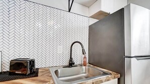 Une cuisine avec un dosseret de carreaux disposés en motif « point de Hongrie », un évier en acier inoxydable, un grille-pain et un réfrigérateur.