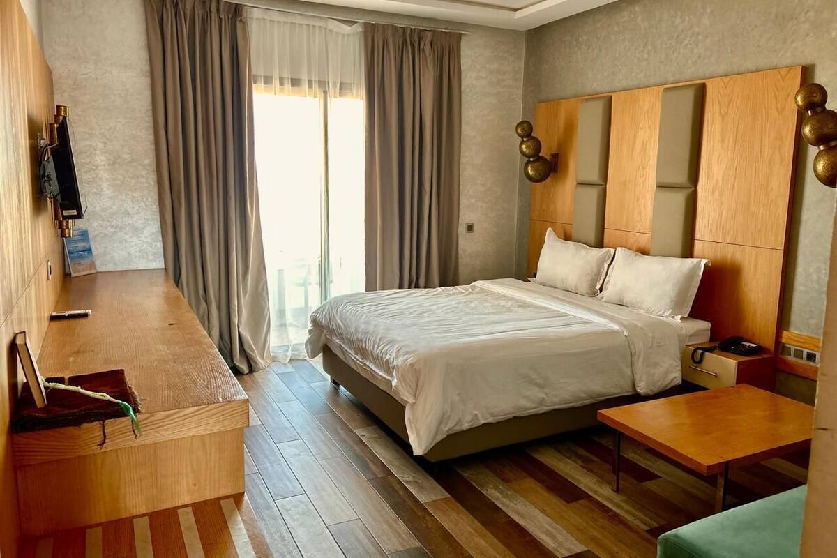 Habitación de hotel con una cama grande, muebles de madera, un escritorio y vistas al exterior.