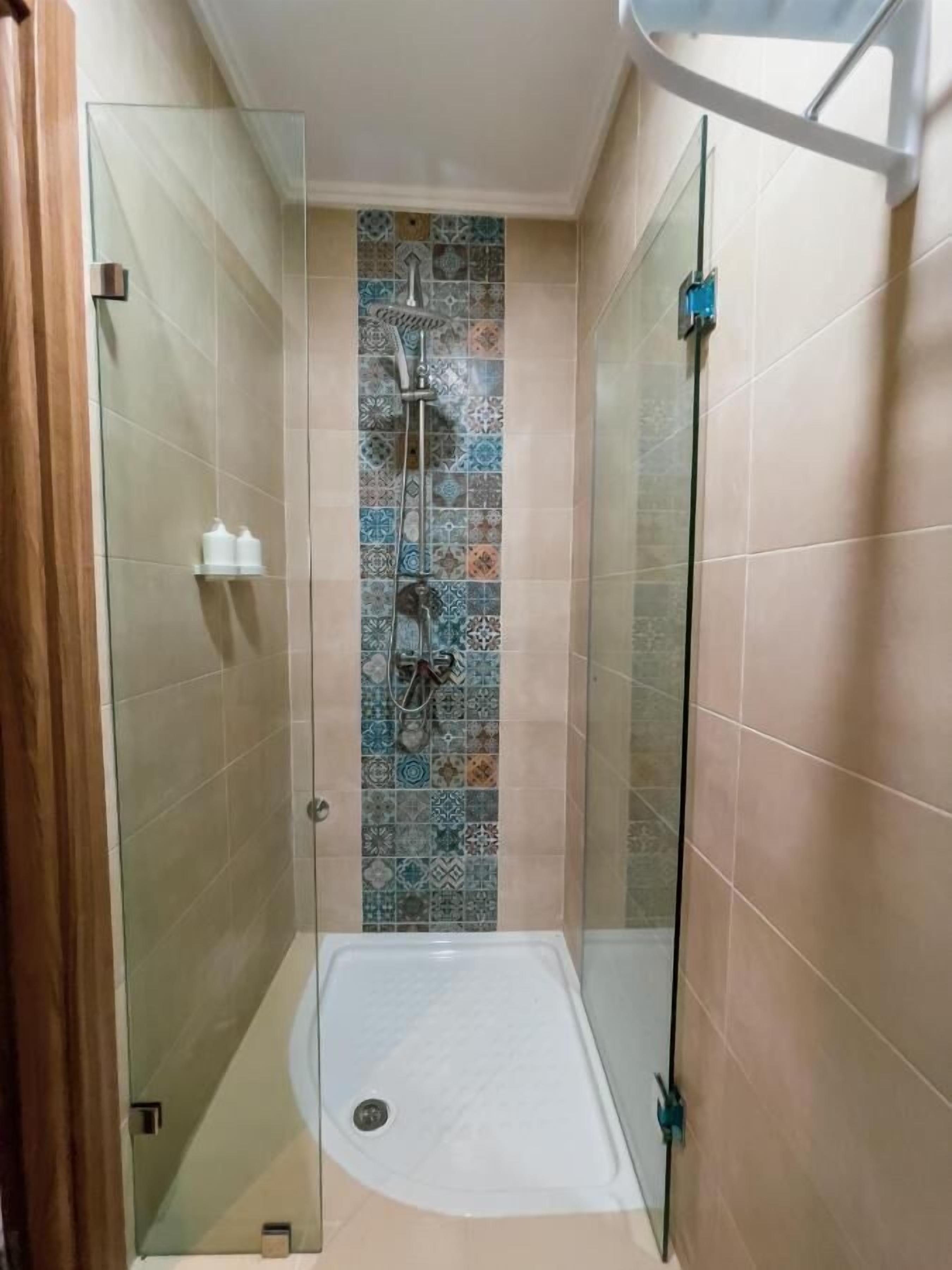A glass-enclosed shower stall with a tiled wall, a handheld showerhead, and a handheld shower attachment.