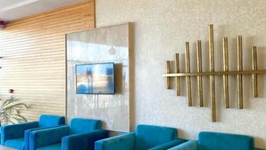 A modern lounge area with blue sofas and wooden tables, a mounted TV, and a decorative wall piece. - Hotel Atlantis Mazagan (Moulay Abdallah)