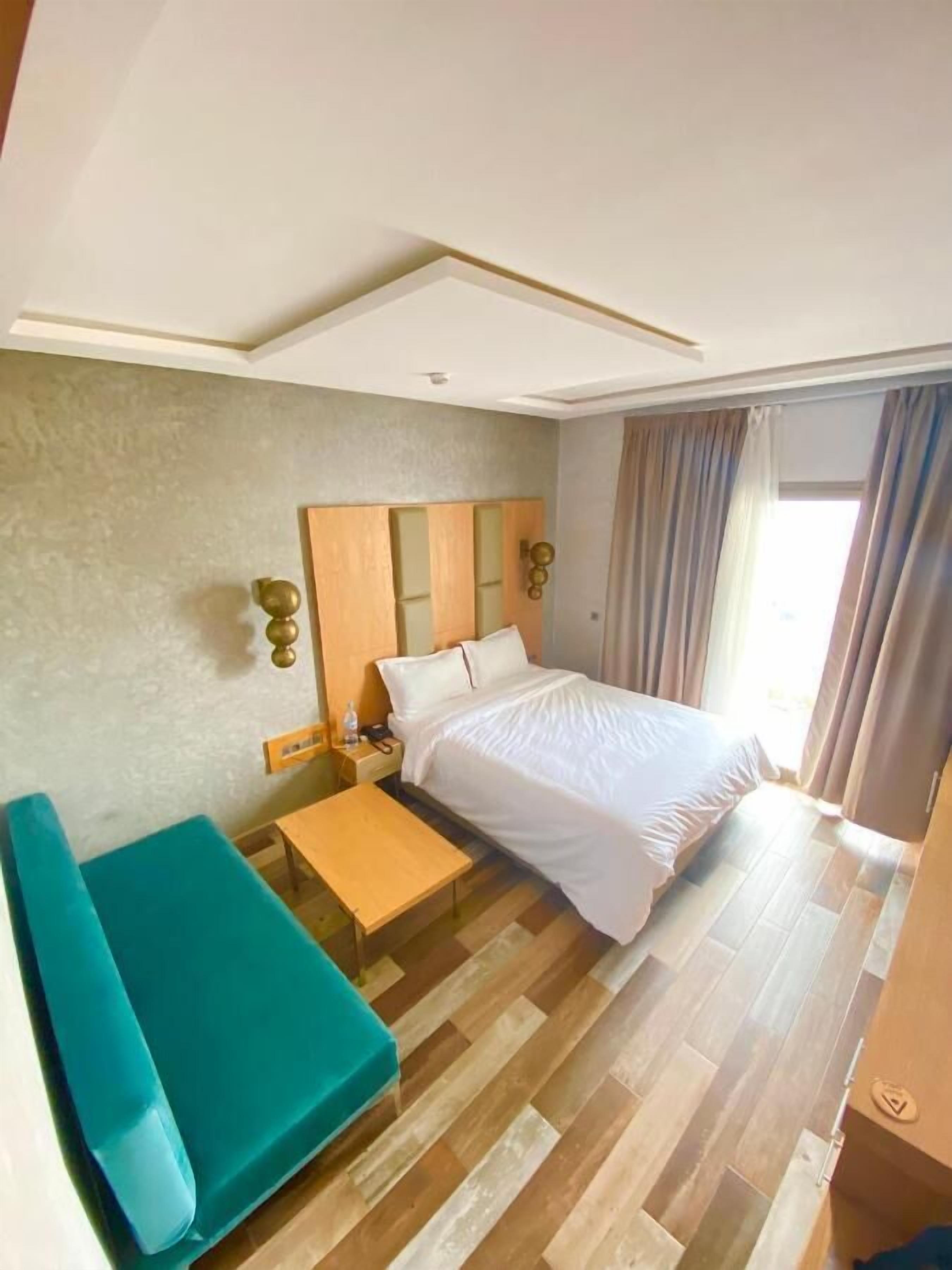 Ein Hotelzimmer mit einem Bett, einem Nachttisch aus Holz, einem blaugrünen Sofa und Holzboden.