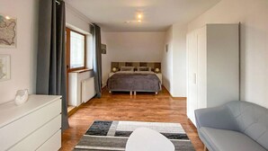 Un dormitorio con cama, mesita de noche, cómoda, sofá y ventana con cortinas.