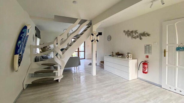 Un interior moderno con una escalera, un mostrador de recepción blanco y un extintor en la pared.