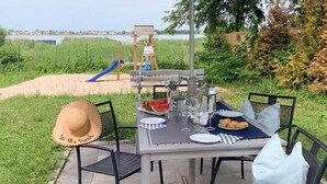 Un espacio de comedor al aire libre con una mesa preparada para dos personas, rodeado de sillas, cerca de un área de juegos con un tobogán.