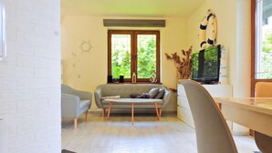 Una sala moderna con un sofá, dos sillones, una mesa de comedor y un televisor.