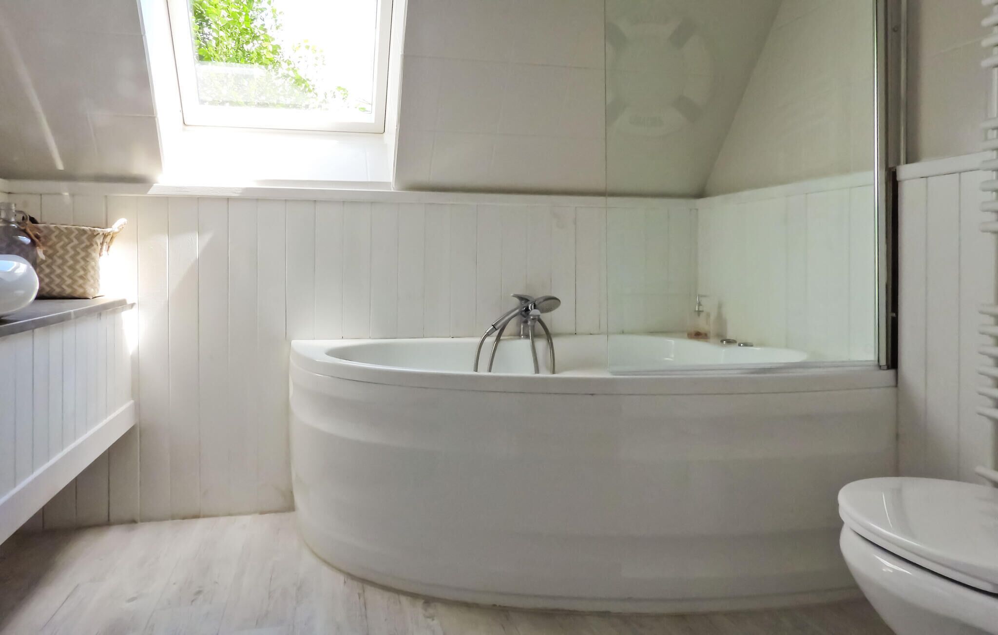 A bathroom with a freestanding bathtub, a toilet, and a window providing natural light.
