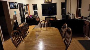 A dining area with a wooden table and chairs, a sofa, a TV, and a fireplace.