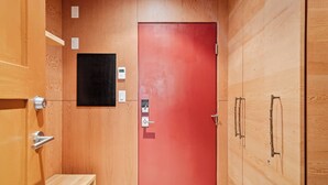 Un interior de madera con una puerta roja, un estante pequeño y un panel negro en la pared.