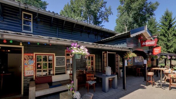 An outdoor café with wooden tables and chairs, a chalkboard menu, and a flower arrangement.