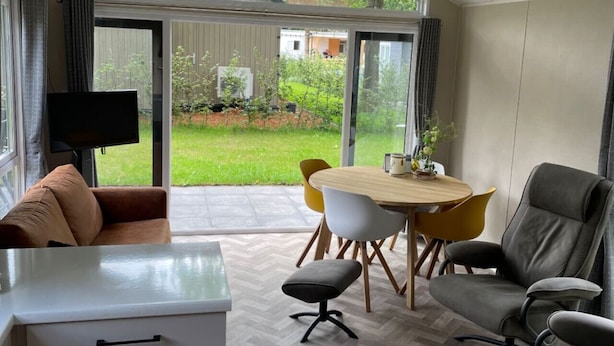Ett modernt rum med en matplats, en soffa, en TV och utsikt över trädgården.