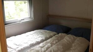 Una camera compatta con un letto singolo, una finestra e una piccola luce a soffitto.