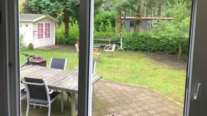 Una vista attraverso una porta di vetro su un giardino sul retro con un tavolo di legno, sedie e un piccolo deposito.