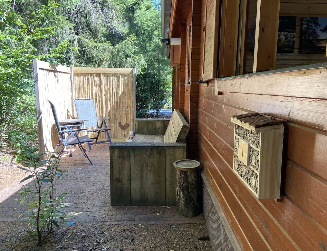 Uma cabana de madeira com uma pequena área de estar ao ar livre, um banco de madeira e uma casa de pássaros na parede.