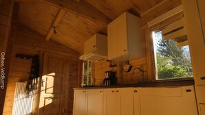 A wooden cabin interior with a kitchen area, including cabinets, a window, and a hanging pot rack. - Tranquility and Natural Beauty Await at Our Secluded Finnish Chalet (Epe)