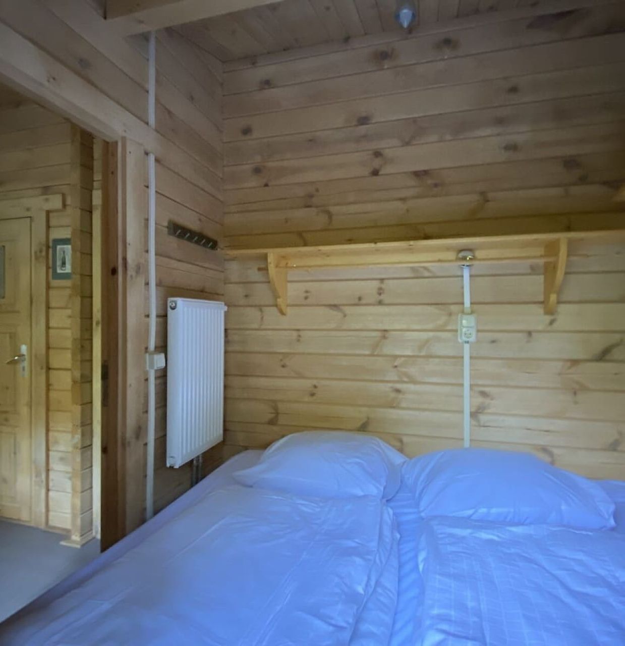 A wooden cabin room with a bed, a radiator, and a door labeled "Oehof, Veldkamp".